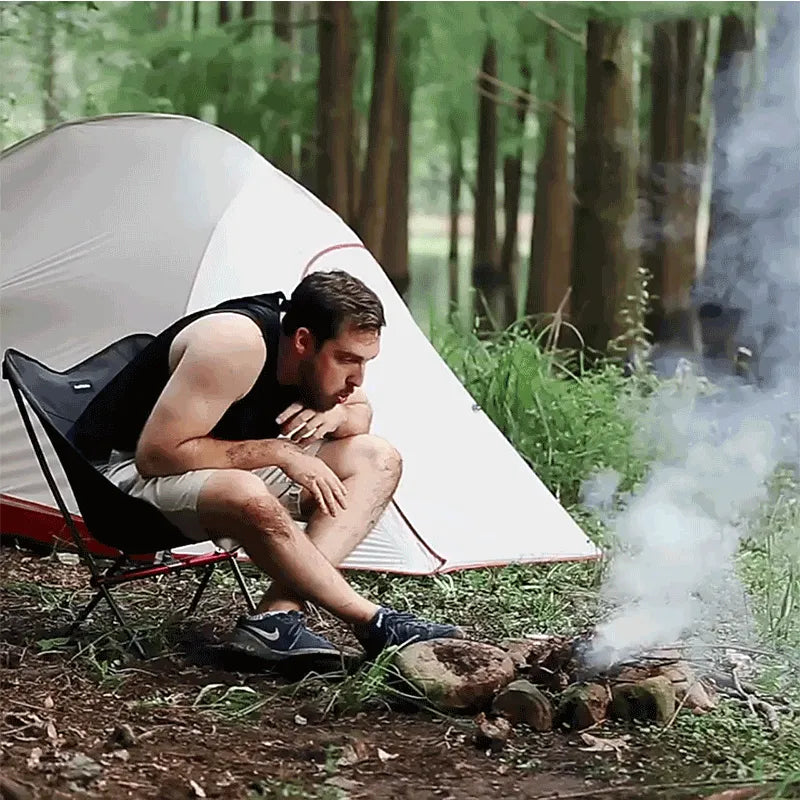 Vista traseira da cadeira premium, destacando a ergonomia e a ventilação em ambiente de acampamento em grupo.