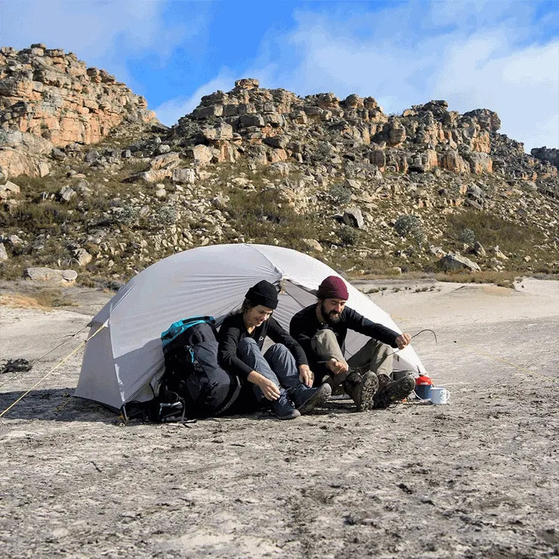 Casal na frente da barraca Mongar Pro em cenário rochoso, representando a experiência premium e a durabilidade em terrenos difíceis de trekking.