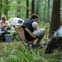 Homem utilizando a cadeira dobrável em ambiente de camping, enfatizando o conforto outdoor e o relaxamento proporcionados pelo design ergonômico.