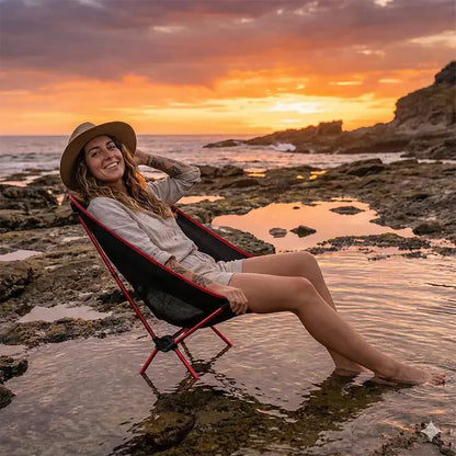 Mulher relaxando em cadeira portátil vermelha na praia durante o pôr do sol