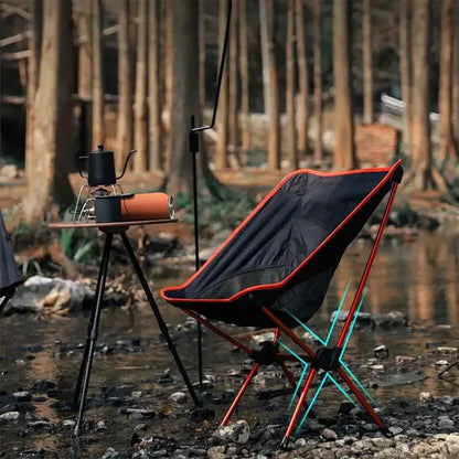 Cadeira portátil vermelha montada na natureza ao lado de riacho e kit de café camping