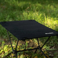 Mesa de camping em gramado, destacando o design compacto e a portabilidade em terrenos leves.