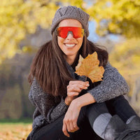 Usuária sorrindo com óculos em cenário de lazer/outono, demonstrando estilo, conforto e proteção solar.