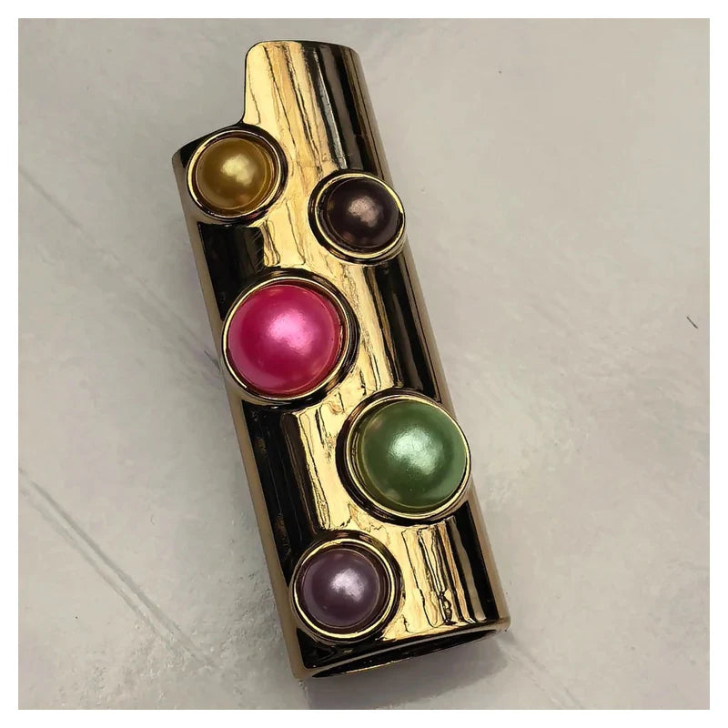 porta-isqueiro-bic-luxo-perolas-coloridas-capa - Porta-isqueiro BIC luxo dourado com perolas coloridas em angulo de capa; isqueiro nao incluso.